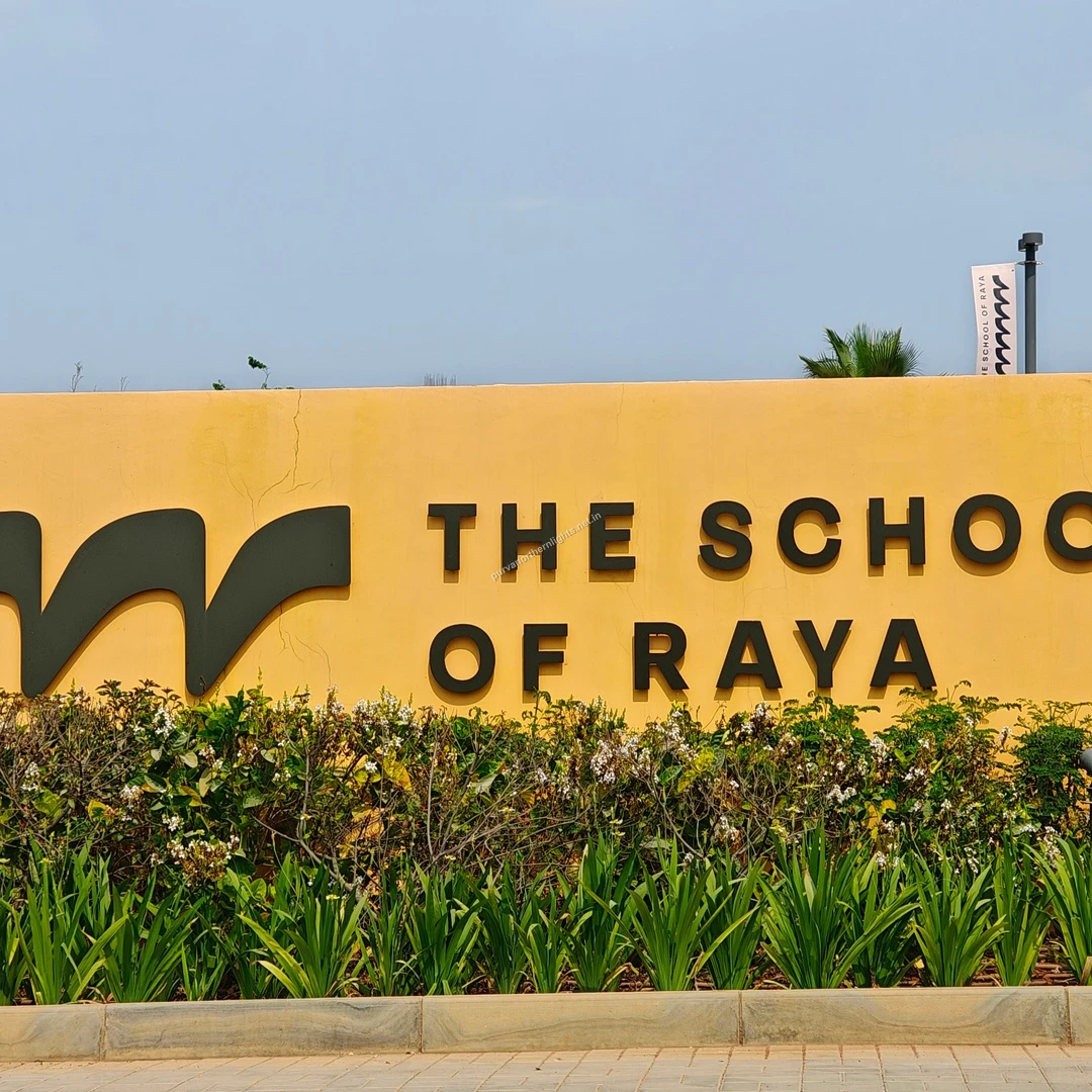 Raya School Facade A clear view of the yellow boundary wall displaying The School of Raya logo and text, surrounded by green plants near Purva Northern Lights.