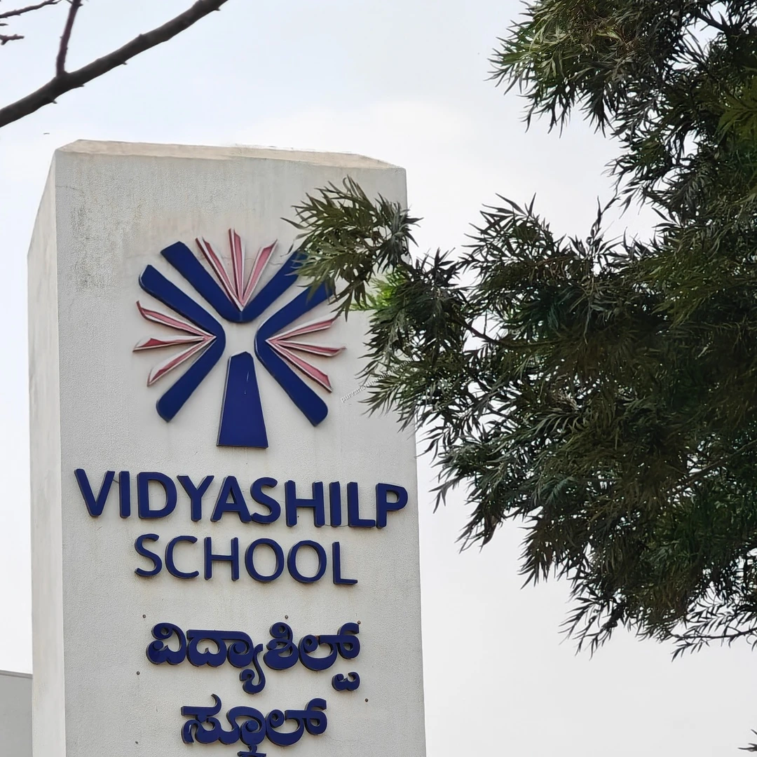 Vidyashilp Entrance Pillar The white concrete pillar displaying the Vidyashilp School logo and name next to leafy branches near Purva Northern Lights.